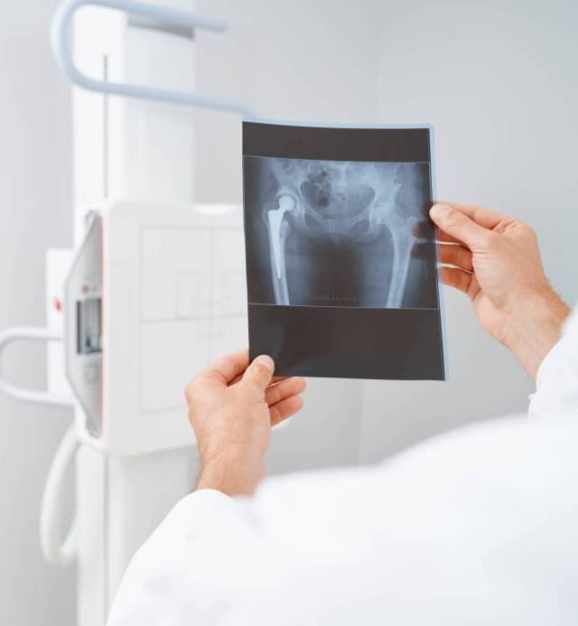 Crop of doctor holding by hands scan after ultrasound diagnostic of pelvis and hip bone. Male radiologist wearing white uniform looking on results of procedure. Concept of modern hospital.